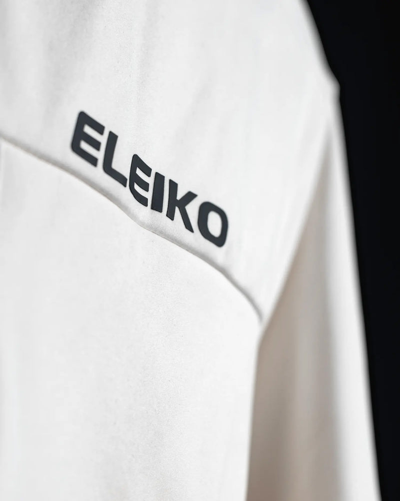 ELEIKO ジャケット ユニセックス ホワイト 胸元を斜めから拡大しELEIKOロゴプリントと生地の質感を確認できるディテール