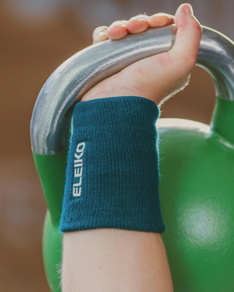 ELEIKO リストバンド ストロングブルーを手首に装着しケトルベルハンドルを握る様子を斜め横から捉えた構図。トレーニング時の汗吸収と手首保護の使用シーンが分かるリストバンド