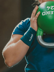 ELEIKO リストバンド ストロングブルーを手首に装着しケトルベルを保持する腕を横から捉えた構図。ELEIKOロゴ刺繍とリブ編み素材のフィット感が分かるトレーニングシーン