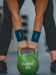 ELEIKO リストバンド ストロングブルーを両手首に装着しケトルベルを両手で持ち上げる動作を正面から捉えた構図。トレーニング中の手首保護と汗止め用途が分かるリストバンド