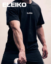 ELEIKO メンズ Tシャツ ブラックを着用した男性の正面上半身。胸元の白いELEIKOロゴと半袖のシルエット、トレーニング時の着用感が分かる