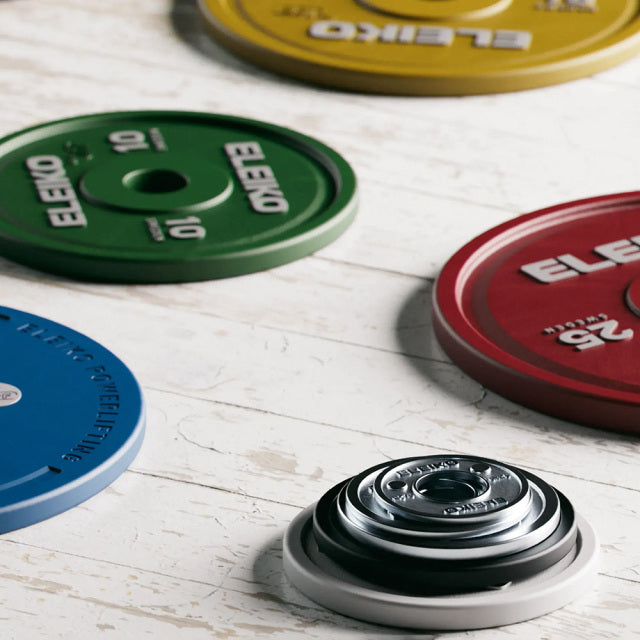 ELEIKO 新型パワーリフティングコンペティションプレート IPF公認品 赤・青・黄・緑 斜め上から捉えた複数プレート配置、各重量カラーのプレート表面ロゴと中央スリーブ穴、IPF公認仕様が分かる全体構成