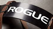 ROGUE アームブラスター レザーストラップ（ブラウン）を上方から捉えた構図で、湾曲した金属プレート中央のロゴとレザーストラップの装着位置が分かる全体像