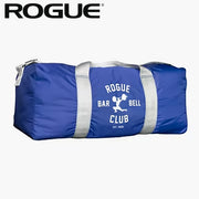 ROGUE オールドスクールジムバッグ ブルー、正面から水平アングルで全体を捉えた構図、中央のROGUE BARBELL CLUBロゴとグレーのストラップ、円筒型ボディが分かる外観デザイン