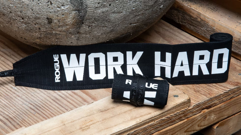 ROGUE ラップ ブラックを木製ベンチ上で斜め上から捉えた構図、WORK HARDプリントと巻いた本体・面ファスナーの厚みが確認できる配置