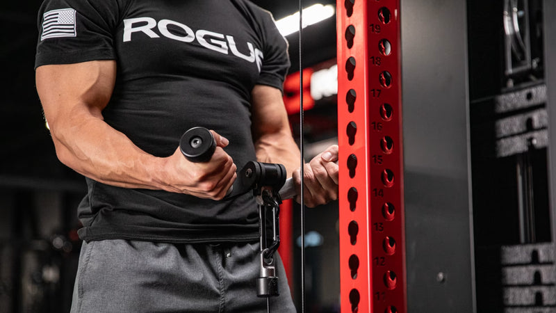 シルバーのROGUE Vグリップ ケーブルアタッチメントを使用し、トライセプスプッシュダウン開始姿勢を正面から捉えた上半身のトレーニングシーン