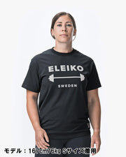 ELEIKO 1957 Tシャツ ユニセックス ブラック 女性モデル正面上半身でロゴとバーベルデザインが中央に配置された着用スタイル