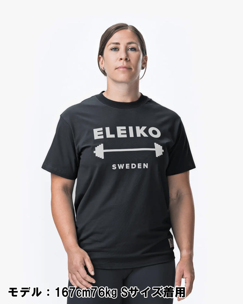 ELEIKO 1957 Tシャツ ユニセックス ブラック 女性モデル正面上半身でロゴとバーベルデザインが中央に配置された着用スタイル