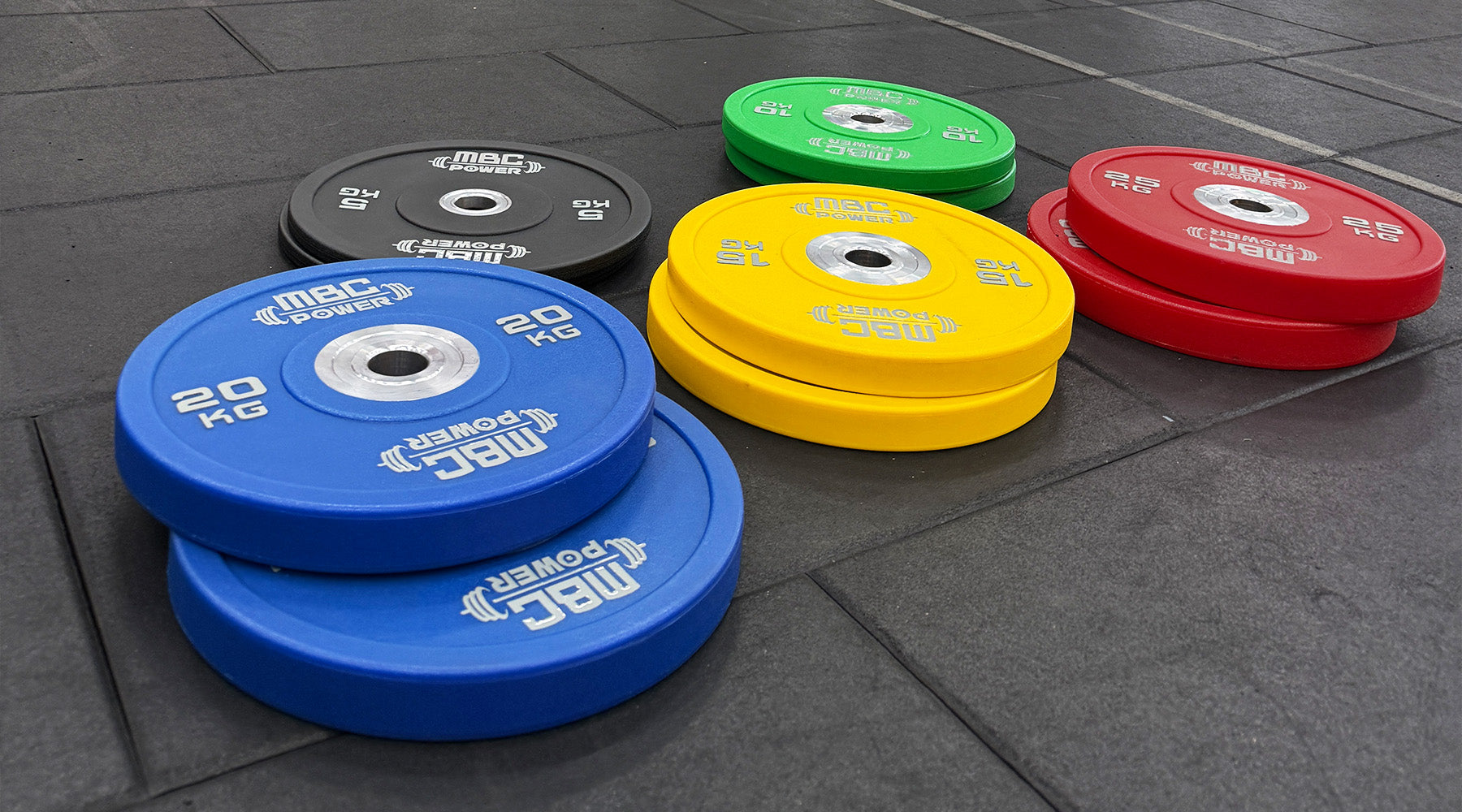 MBC ウレタンバンパープレート ブルー20kg・イエロー15kg・レッド25kg・グリーン10kg・ブラック5kgを床に並べた斜め低位置からの視点、カラー別重量構成が分かる構図