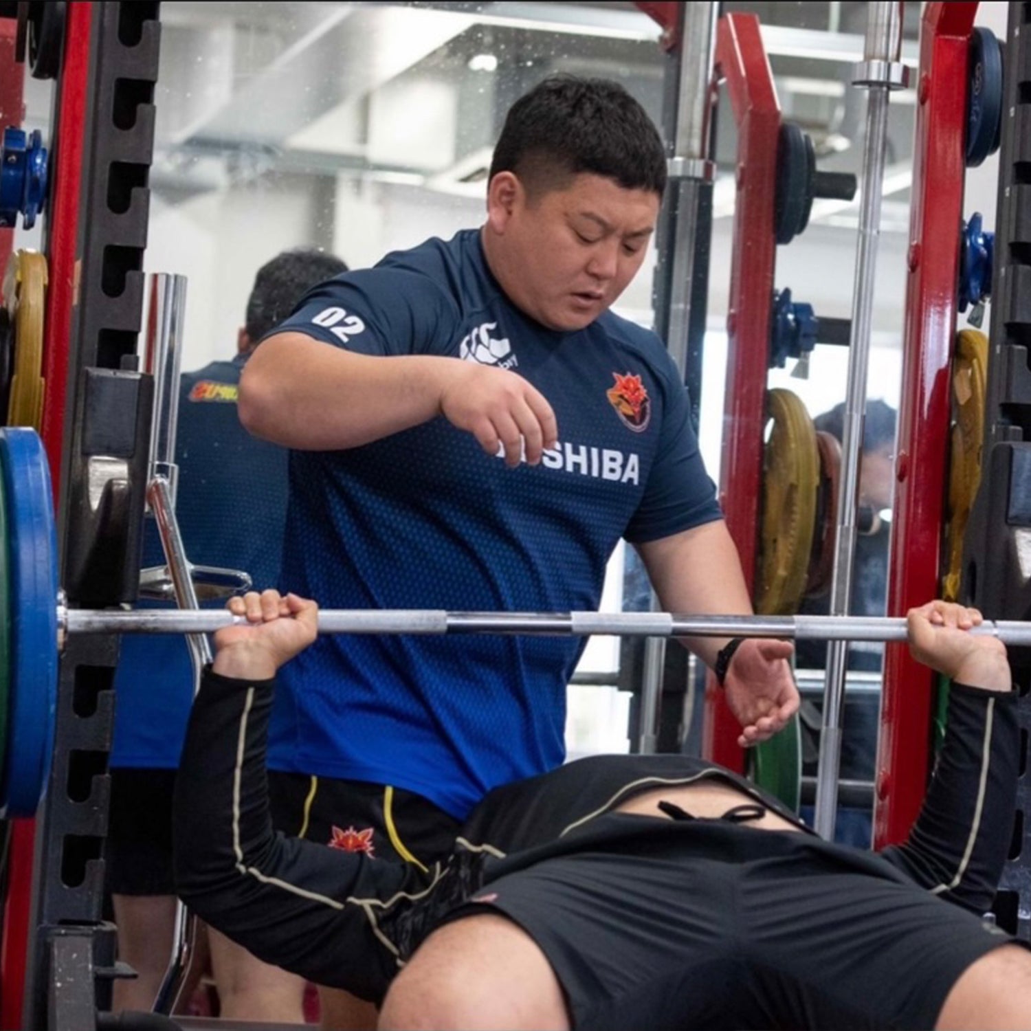 木下進人オンラインパーソナル 青色ウェアのトレーナーがベンチプレスを補助する正面からの視点でラックと動作全体を捉えた指導シーン