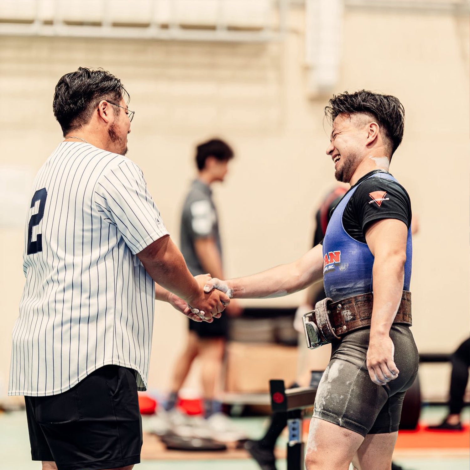中澤 悠人オンラインパーソナル 白色トップスと青色シングレットの選手が横から握手する様子を全身で捉え関係性が分かる構図